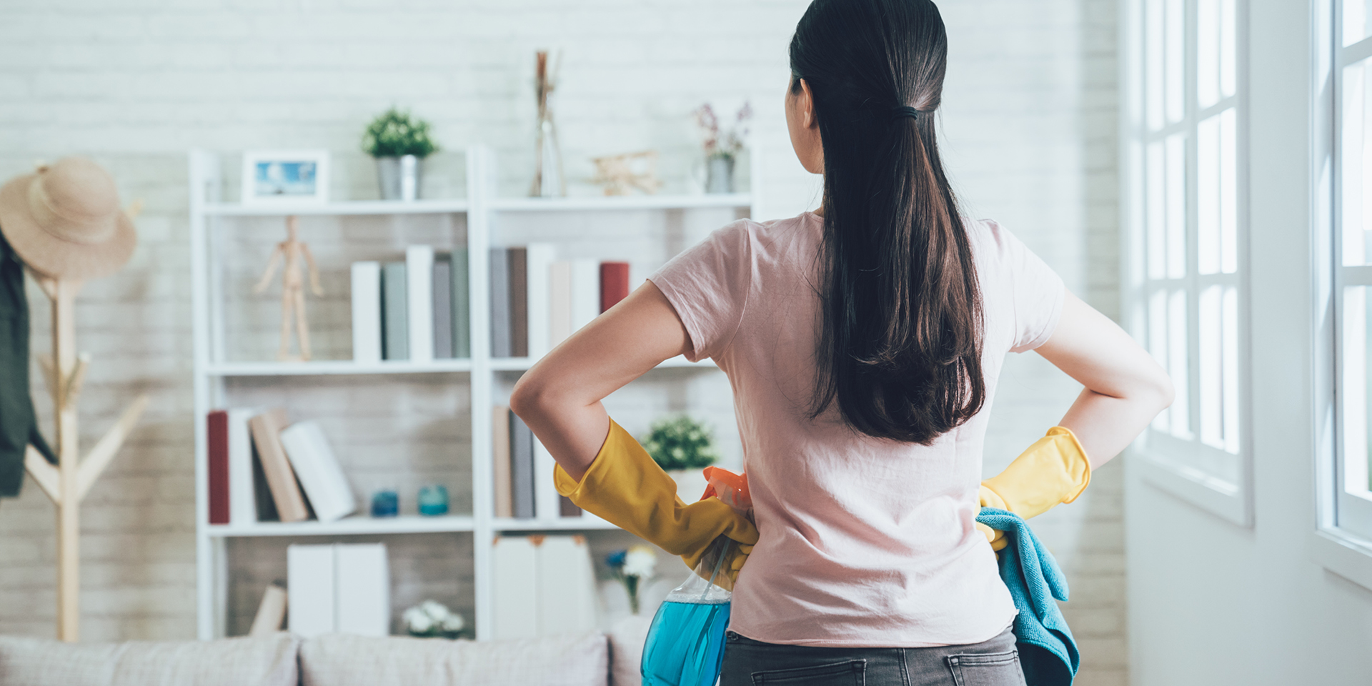 Woman with rubber gloves and hands on hips looks at her bookshelf